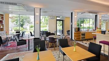 Eine moderne Hotelhalle mit einer zentralen Sitzecke, einer Rezeption und großen Fenstern mit Blick ins Freie.