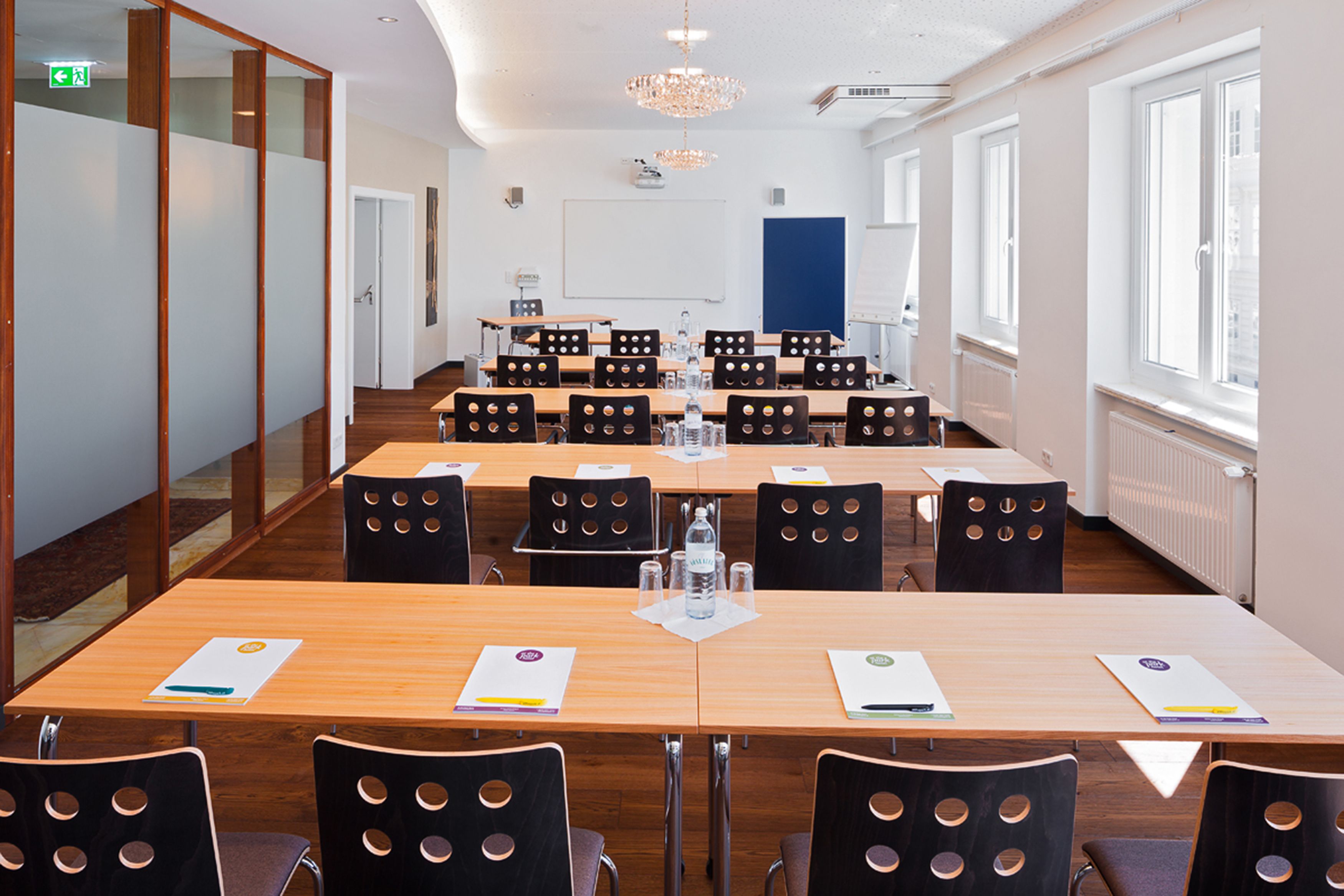 A conference room with long tables and chairs, a whiteboard, and a chandelier.