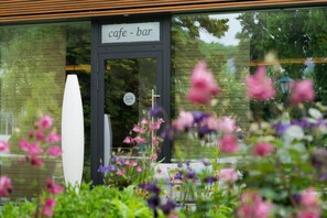 A cafe-bar with a sign above the entrance, a white vase, and flowers in the foreground.