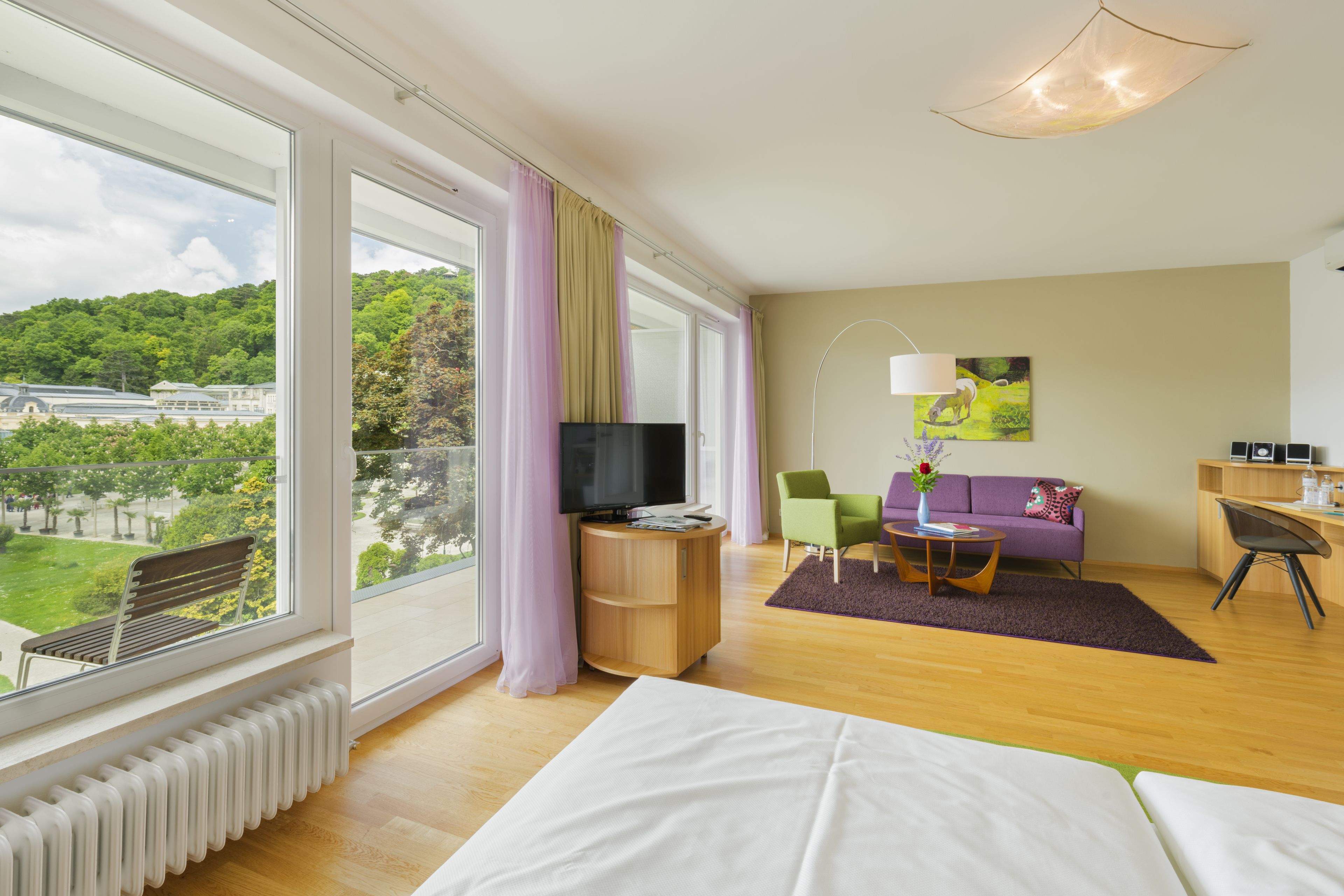 Quarto de hotel moderno com uma grande janela, televisão de tela plana, sofá, escrivaninha e cama.