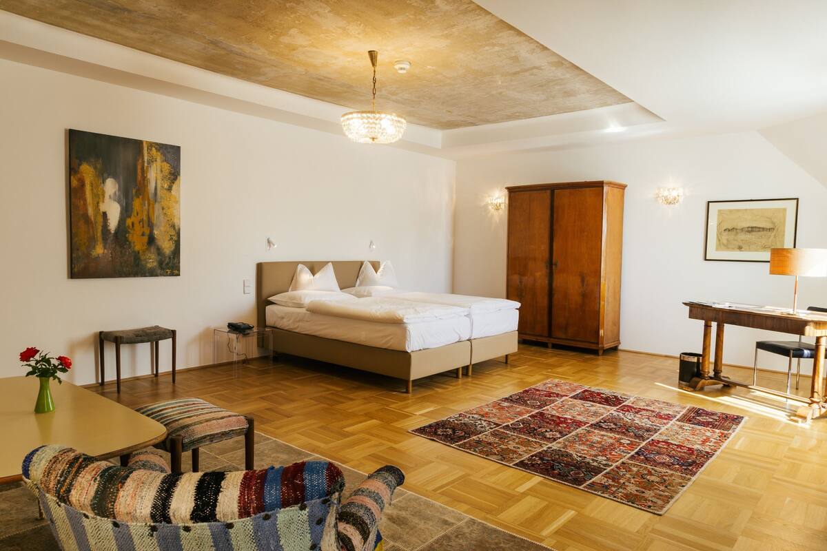 Ein Schlafzimmer mit einem Bett, einem Holzschrank, einem Schreibtisch und einem Esstisch mit Stühlen.