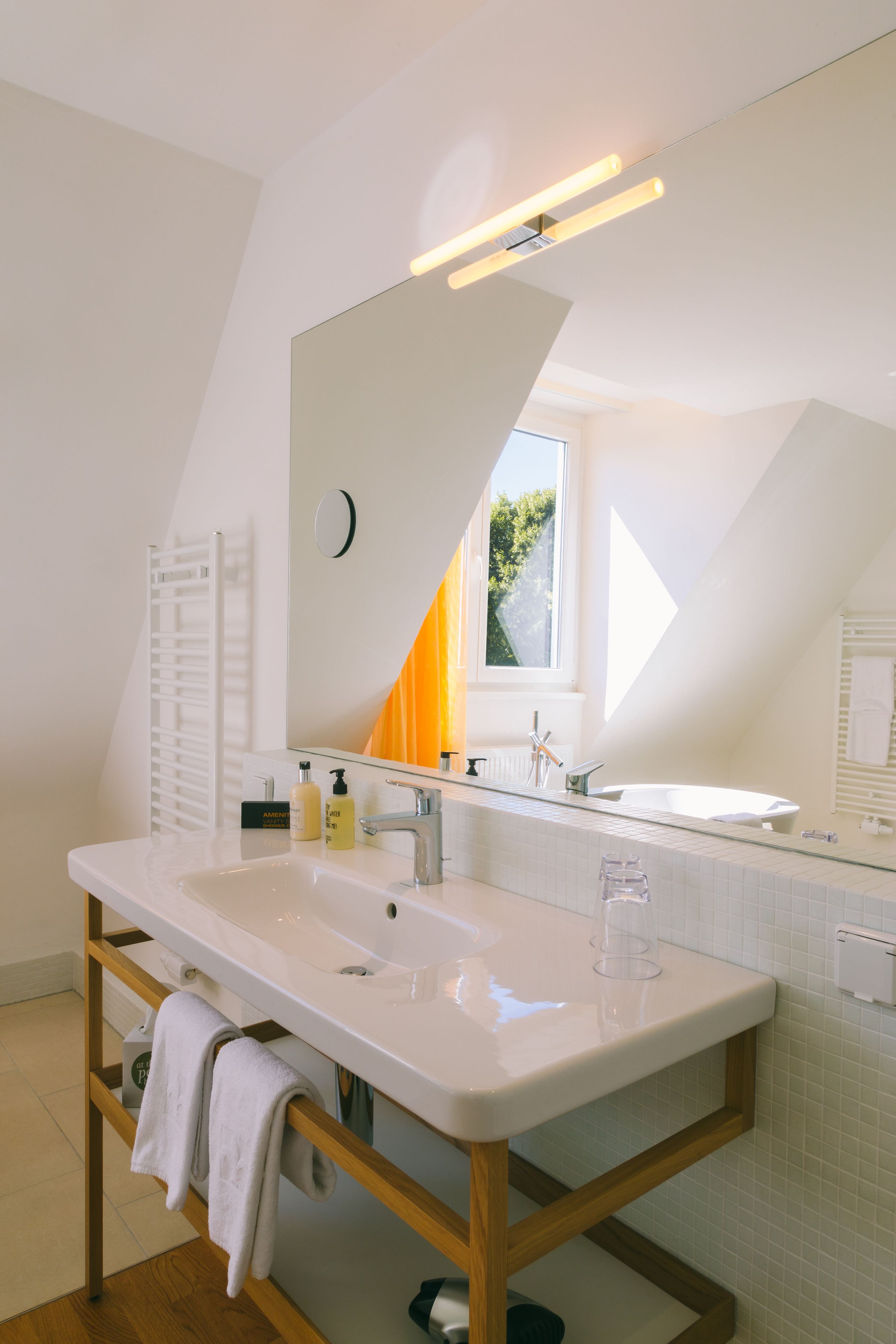 Ein modernes Badezimmer mit einem großen, weißen Waschbecken, einem Spiegel und einem Fenster.