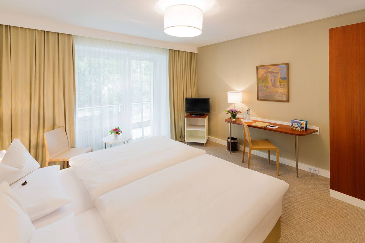 Ein Hotelzimmer mit zwei Betten, einem Schreibtisch, einem Fernseher und einem Bild an der Wand.