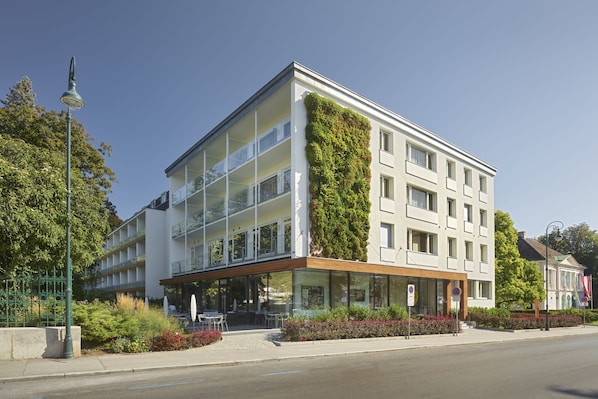 A modern building with a glass facade, a green vertical garden, and a covered outdoor seating area.