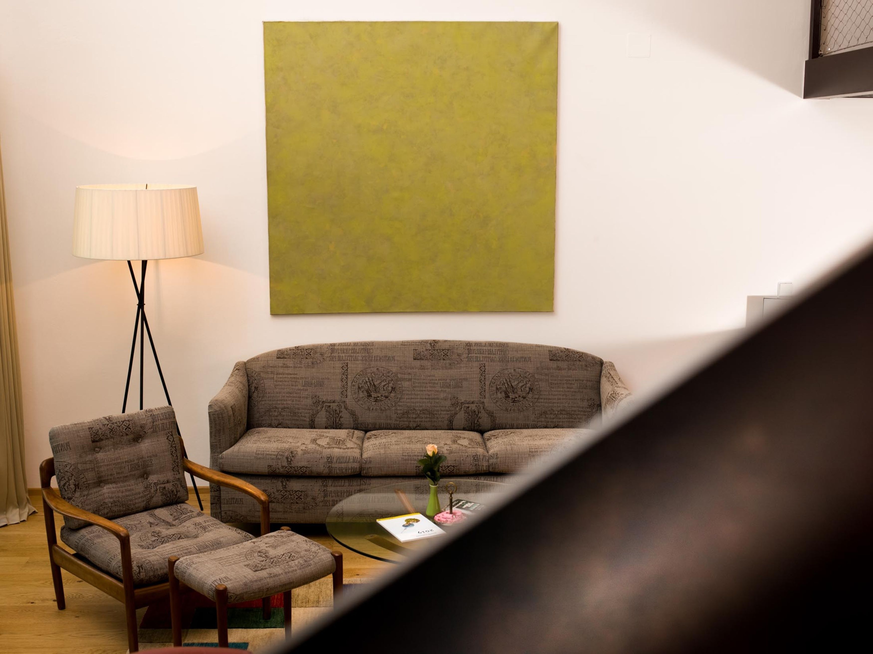 Una sala de estar con un sofá, dos sillones, una lámpara de pie y una mesa de centro con un libro y flores.