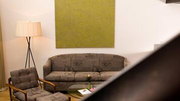 Una sala de estar con un sofá, dos sillones, una lámpara de pie y una mesa de centro con un libro y flores.