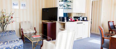 Habitación de hotel con sala de estar, mesa de comedor, televisor y cocina.