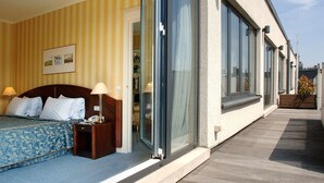 A hotel room with a bed, bedside lamps, a wooden nightstand, and a large sliding glass door leading to a balcony.