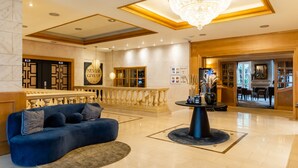 A spacious lobby with a blue sofa, a chandelier, and a reception desk.