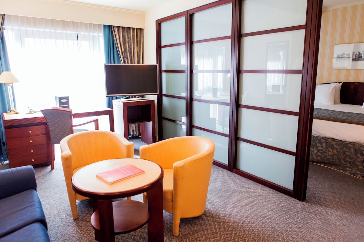 A hotel room with a sofa, a small table with a book, a TV, a bookshelf, and a large sliding door.