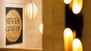 A hotel lobby with a 'NEVER GIVE UP' poster, a modern light fixture, and a stone balustrade.