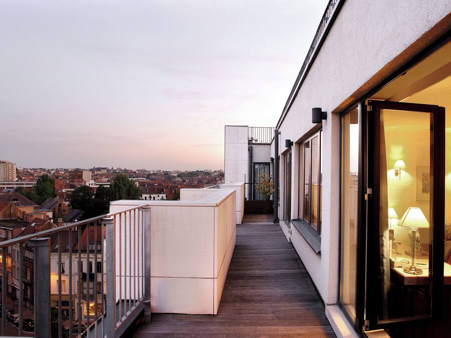 Un balcón moderno de hotel con suelo de madera, un área de descanso con mesa y sillas, y vista a la ciudad.