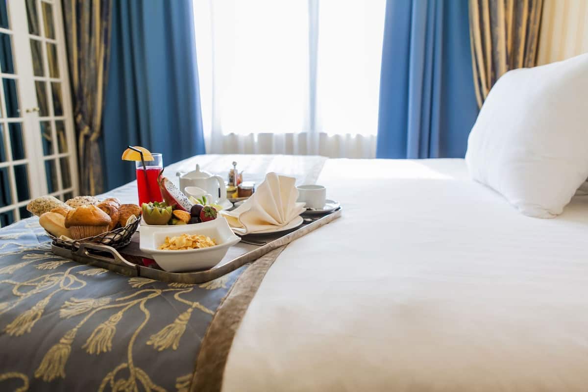 A hotel room with a neatly made bed, a tray with breakfast items, and a window with curtains.