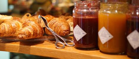 A display of croissants and jars of jam and orange juice on a wooden counter.