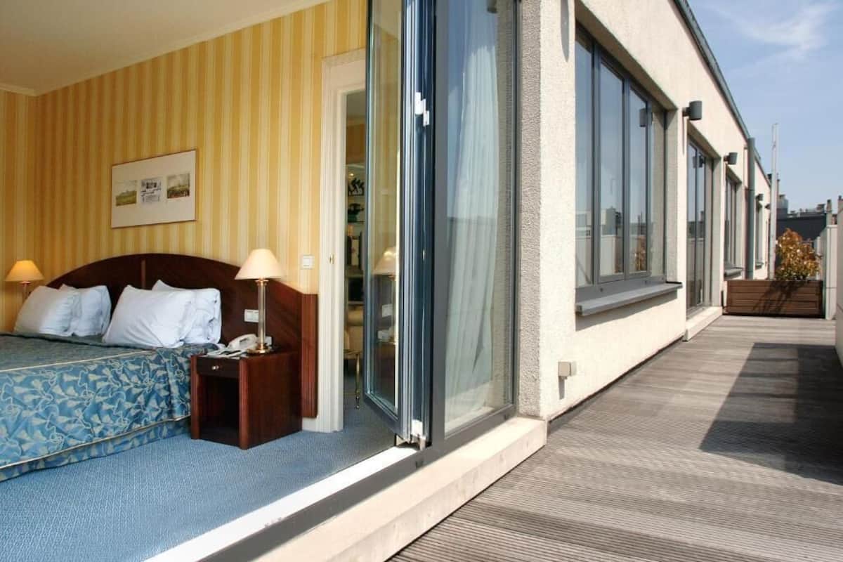 A hotel room with a bed, bedside lamps, a nightstand, and a large sliding glass door leading to a balcony.