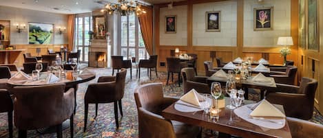 Un comedor de hotel con varias mesas dispuestas para los huéspedes, que presenta una alfombra estampada y un candelabro.