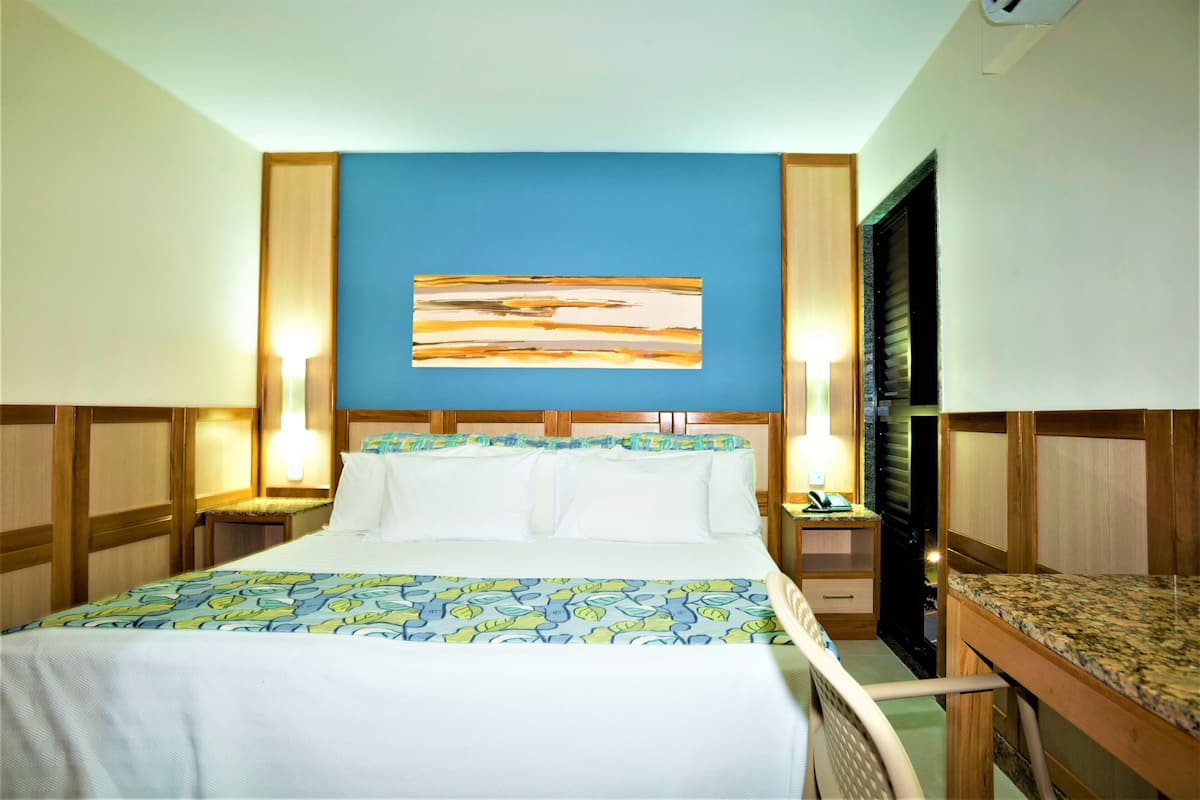 A hotel room with a bed, a desk, and a wall-mounted artwork.