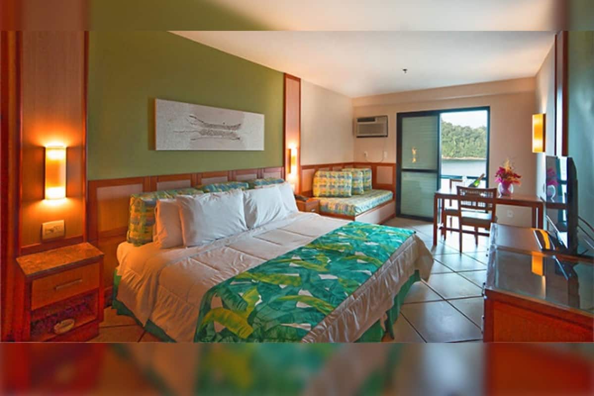A hotel room with a bed, a desk, a chair, a nightstand, and a window with a view.