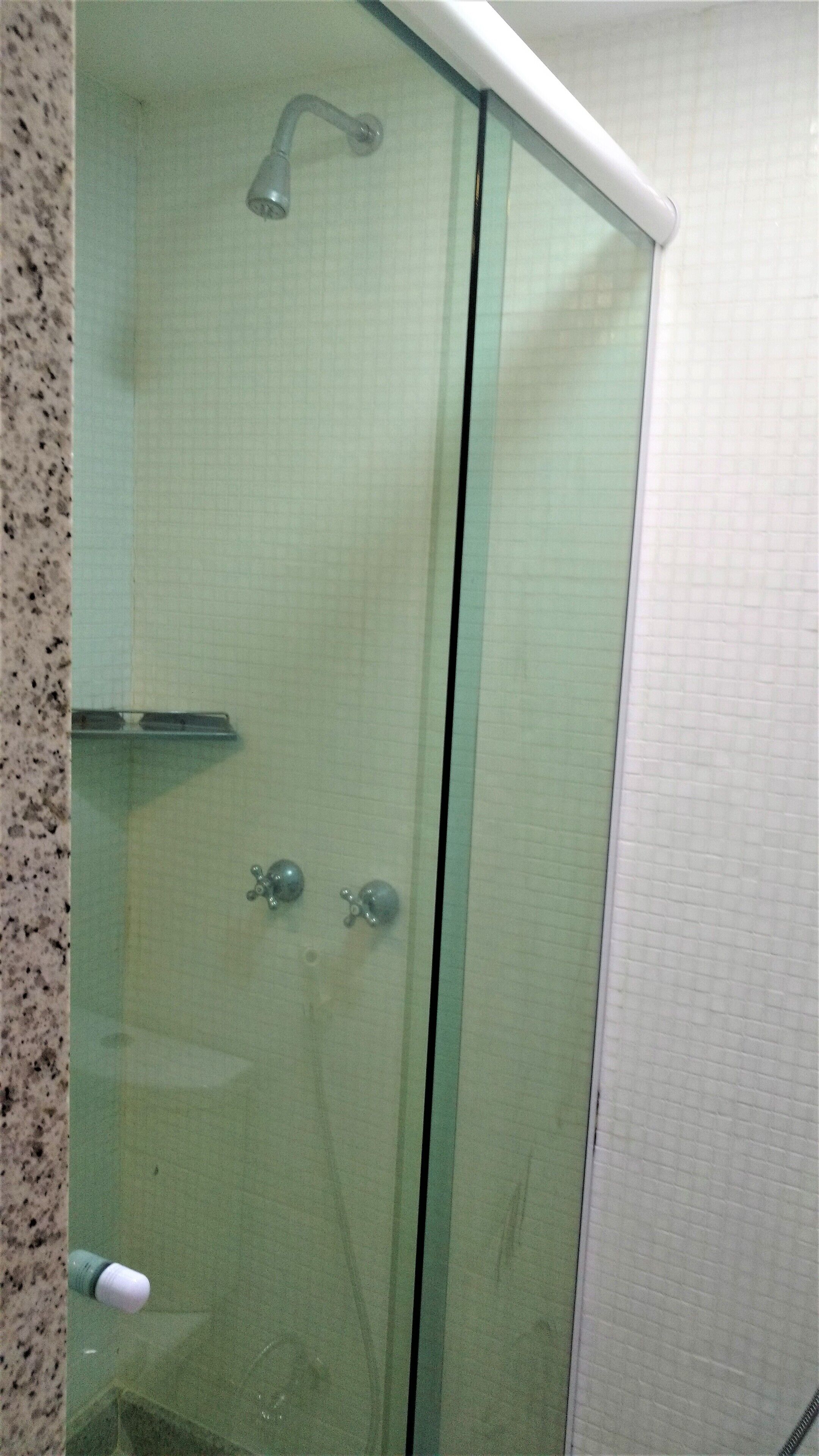 Cabina de ducha con paredes de vidrio, cabezal de ducha de mano y grifo de mano.