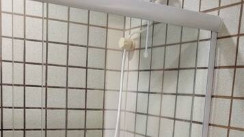 Ducha con puerta de vidrio, inodoro y un rollo de papel higiénico en su soporte.