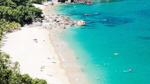 Uma praia com águas turquesa cristalinas, areal arenoso e um cais que se estende para dentro do mar.