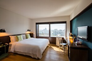 Une chambre d’hôtel avec un grand lit, un bureau avec une chaise, une télévision et une fenêtre donnant sur la ville.