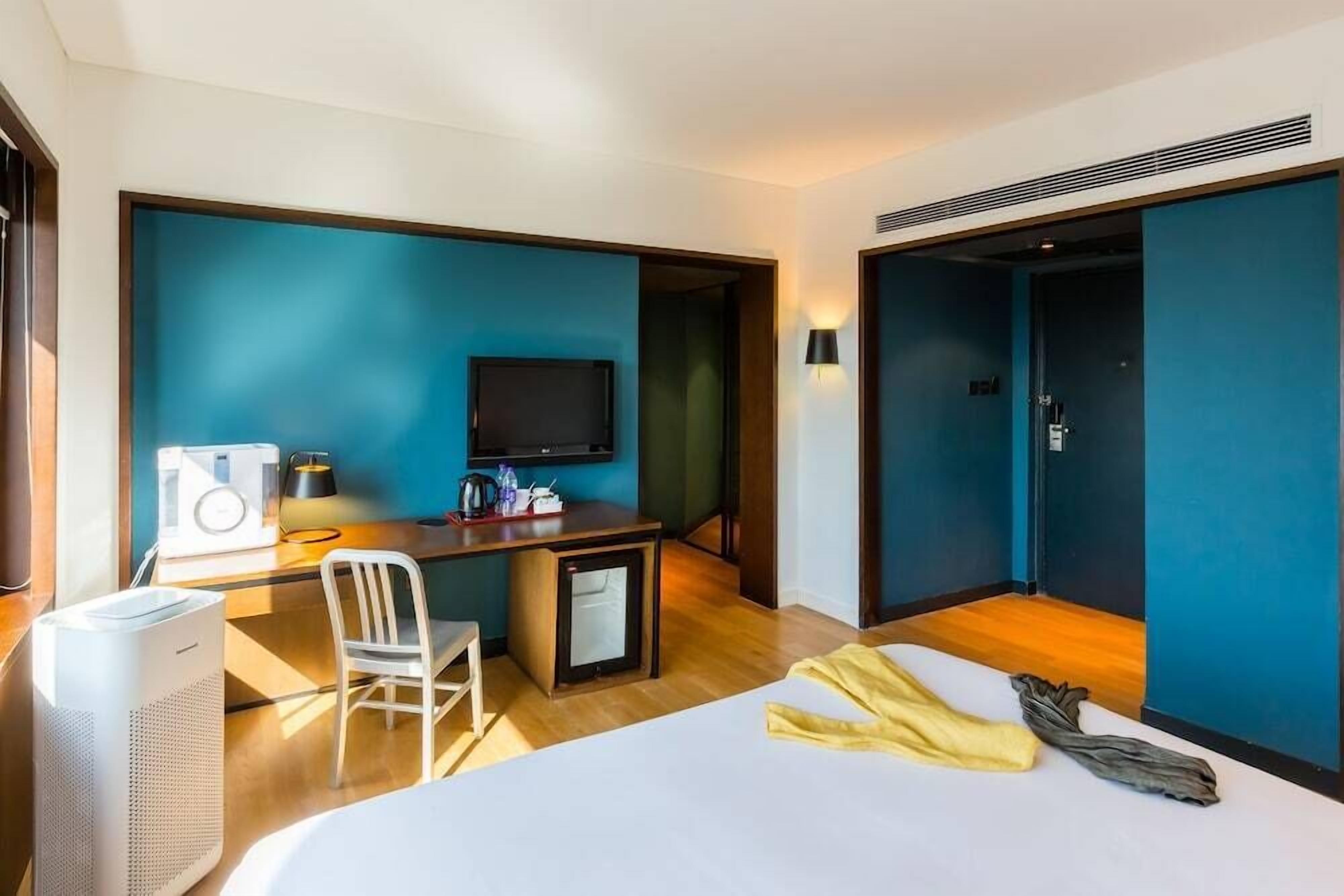 Ein Hotelzimmer mit Bett, Schreibtisch, Stuhl, Fernseher und kleinem Kühlschrank.