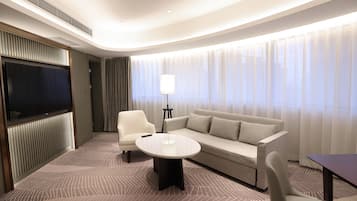Une chambre d’hôtel moderne équipée d’un grand téléviseur à écran plat fixé au mur, d’un canapé, d’une table basse et d’une lampe.