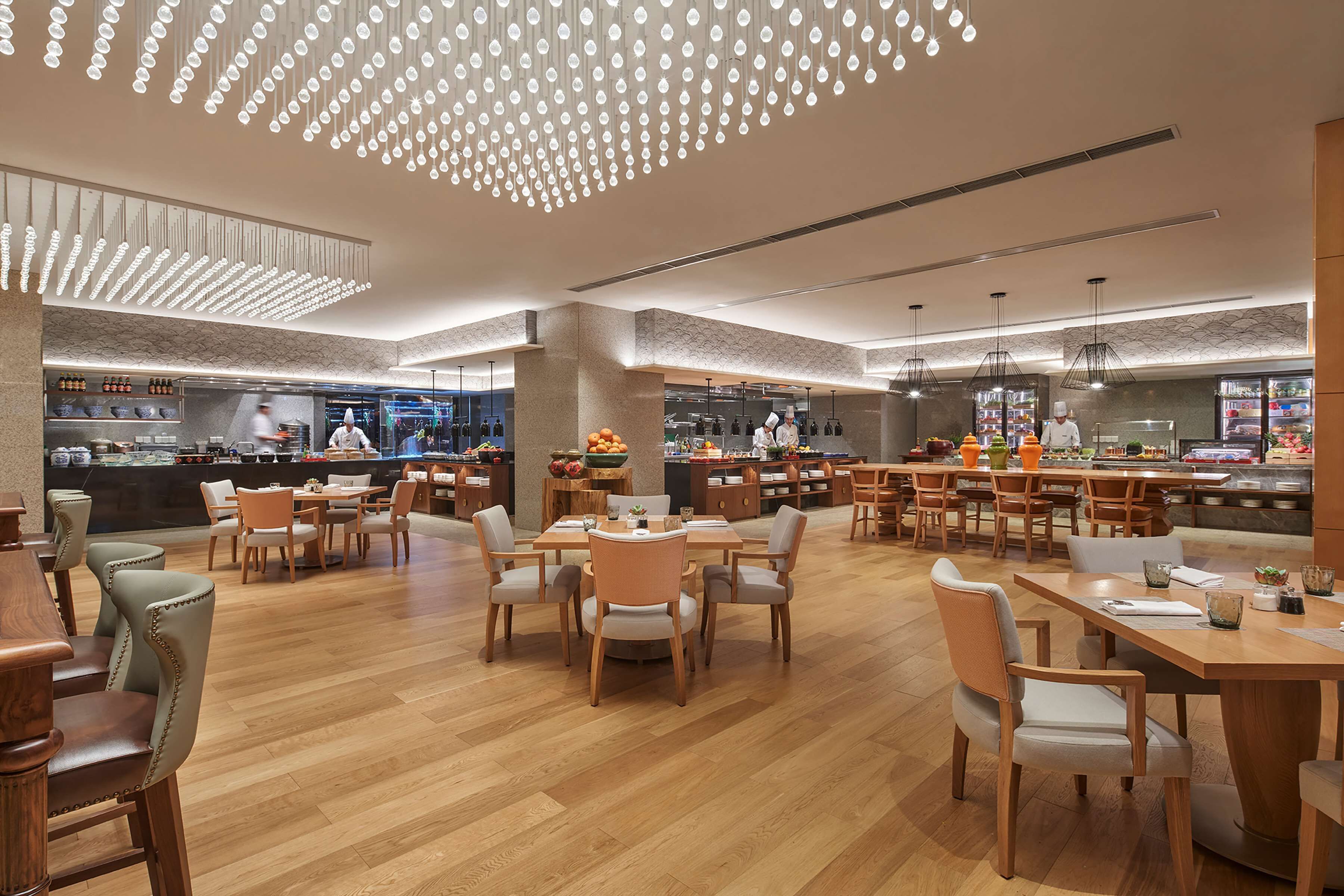 Un restaurante espacioso con mesas y sillas de madera, un diseño moderno en el techo y una zona de cocina a la vista.