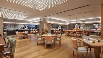 Un restaurante espacioso con mesas y sillas de madera, un diseño moderno en el techo y una zona de cocina a la vista.
