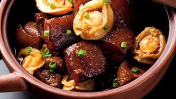 Un bol de nourriture avec un couvercle, contenant ce qui semble être un ragoût ou un curry avec des morceaux de viande, et garni d’oignons verts.