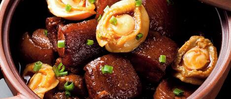 Un bol de nourriture avec un couvercle, contenant ce qui semble être un ragoût ou un curry avec des morceaux de viande, et garni d’oignons verts.