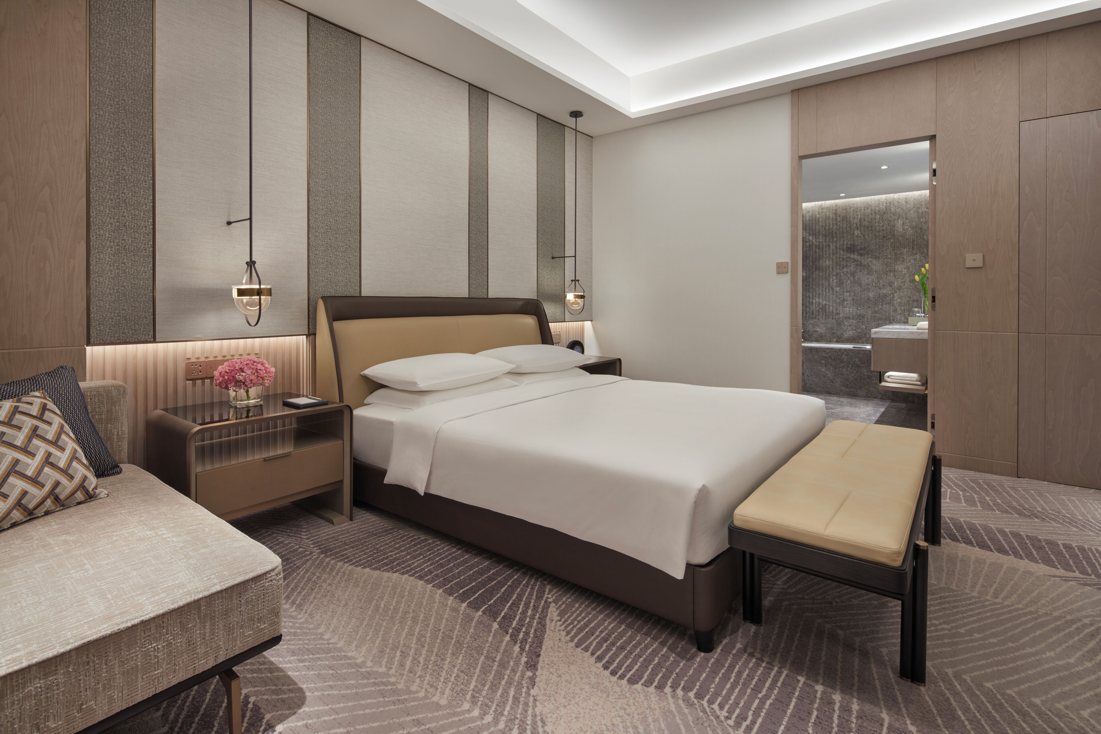 A modern hotel room with a large bed, bedside tables with lamps, a bench, and a mirror.
