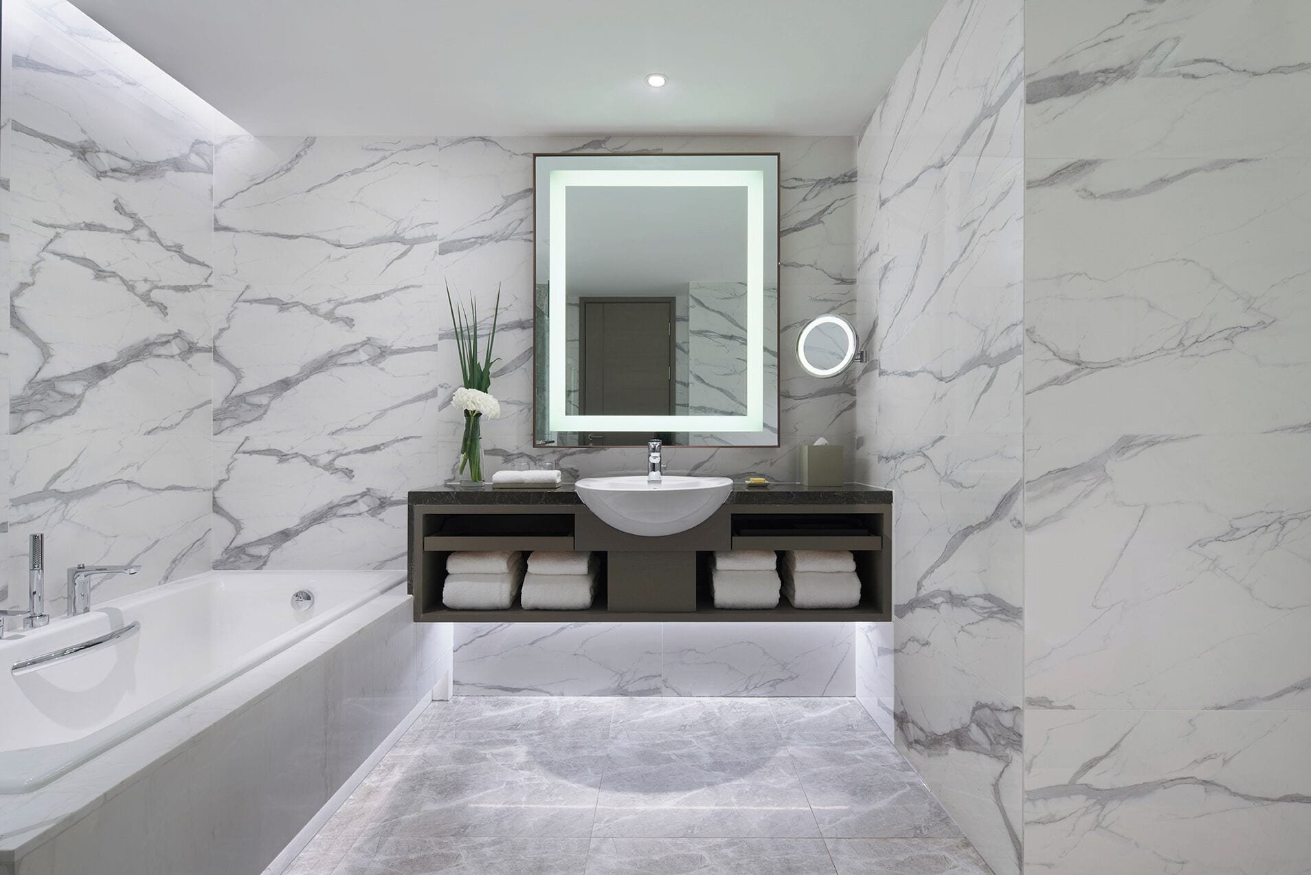 Un baño moderno con salpicadero de mármol, un espejo grande, un lavamanos, una bañera y un perchero para toallas.