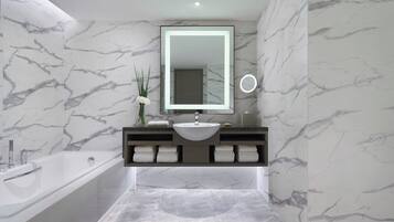 Un baño moderno con salpicadero de mármol, un espejo grande, un lavamanos, una bañera y un perchero para toallas.