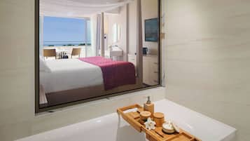 A hotel room with a bed, a bathroom with a bathtub, and a view of the ocean.