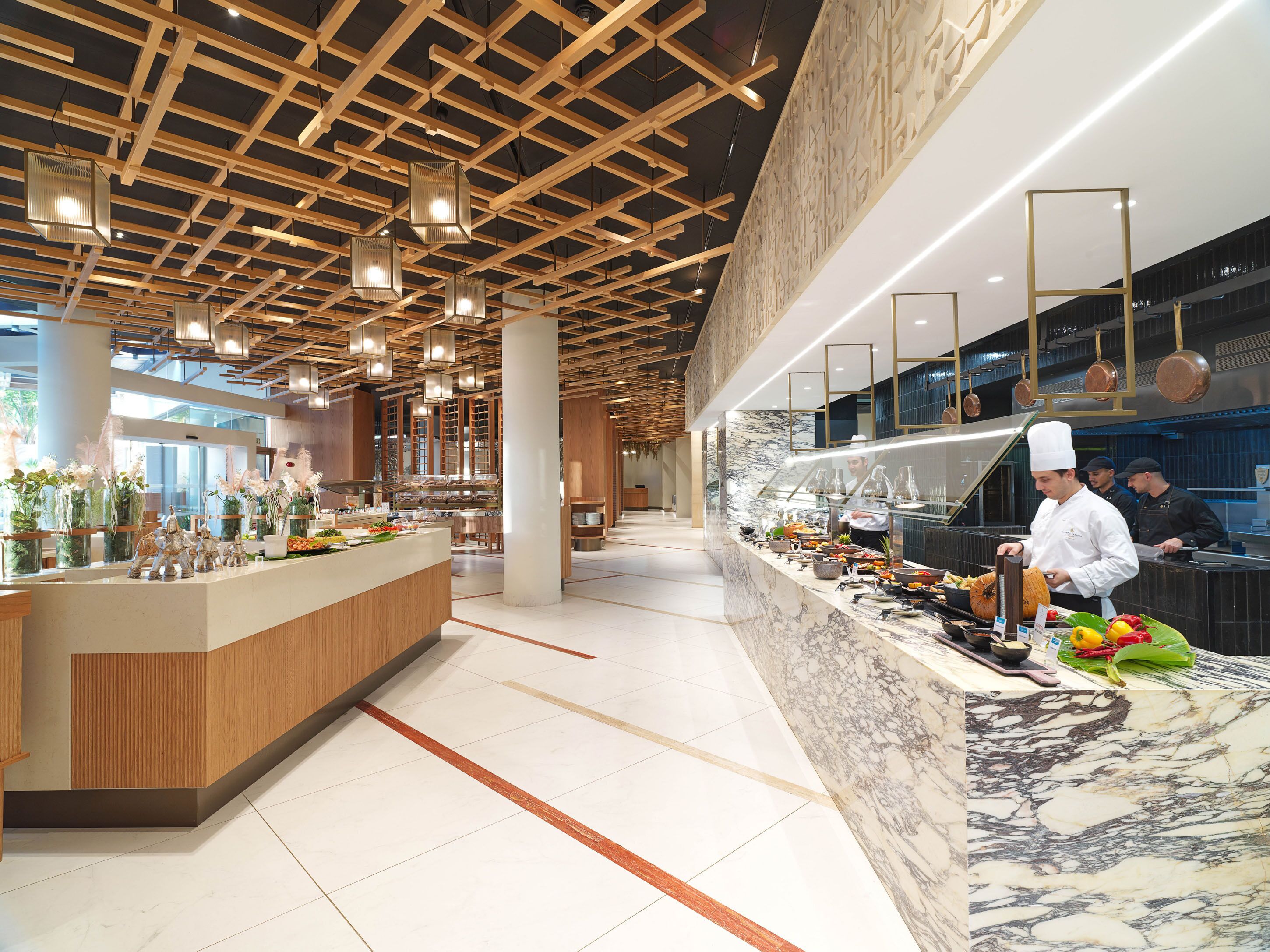 A modern kitchen with a marble countertop, wooden ceiling, and hanging lights.