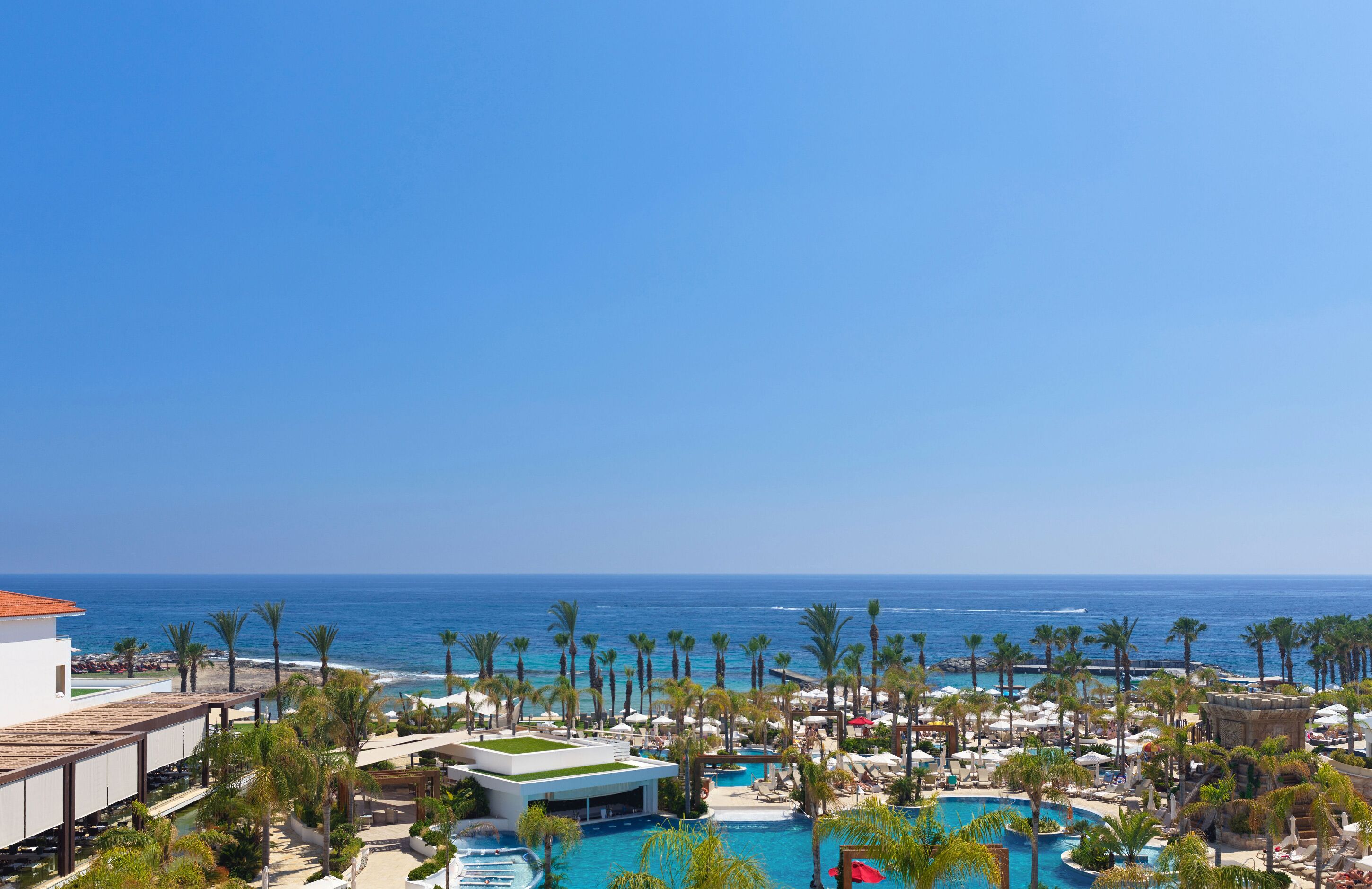 A resort with multiple swimming pools, palm trees, and a view of the ocean.