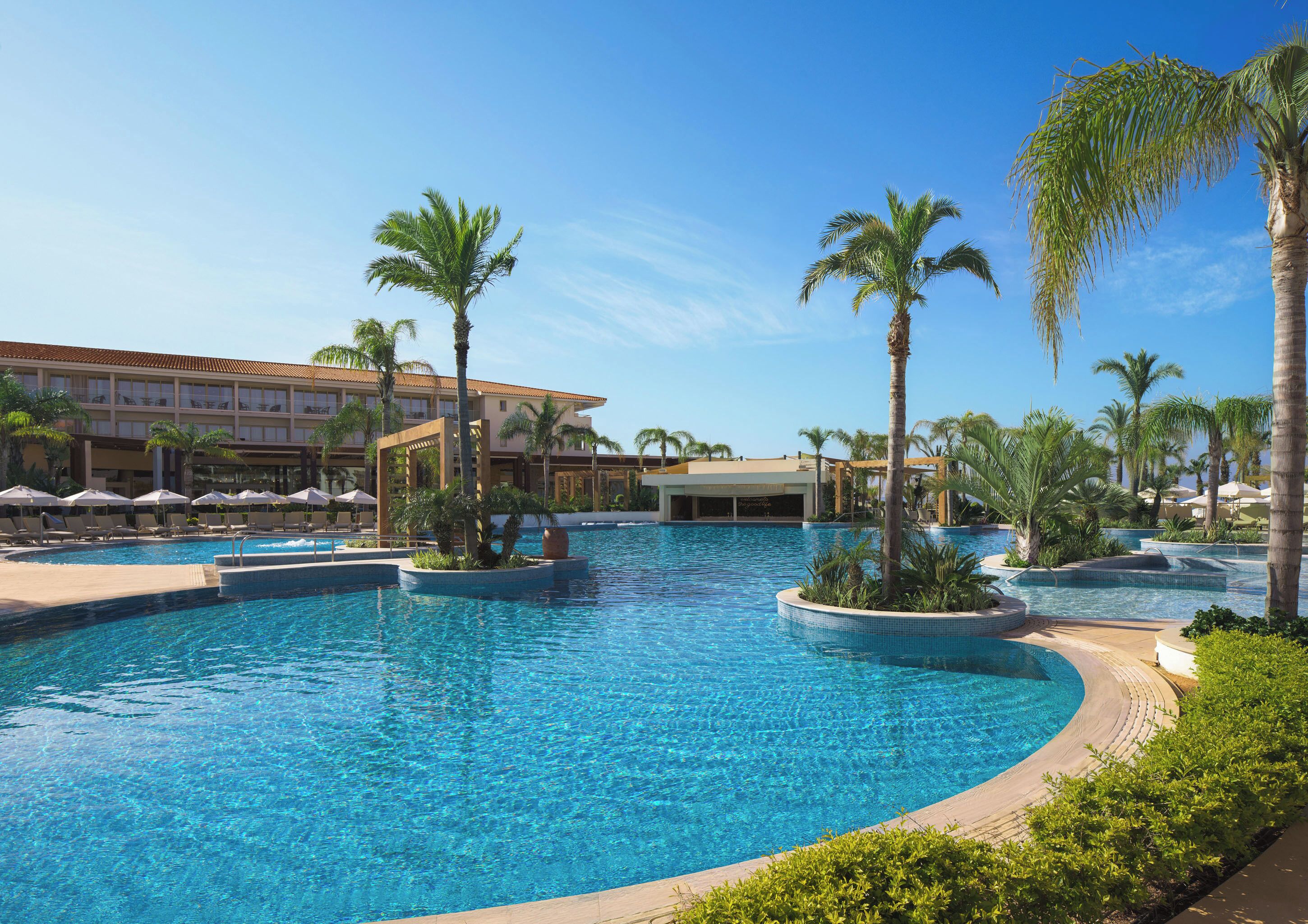 A resort pool area with palm trees, lounge chairs, and a building with multiple floors.