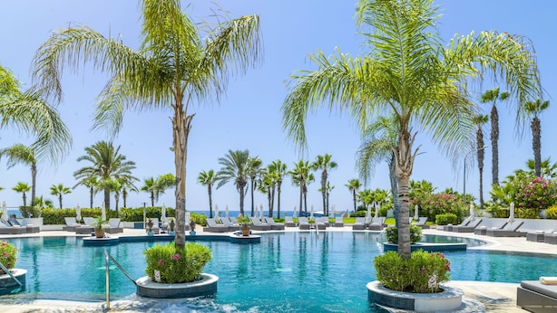 A pool area with lounge chairs and palm trees. - Olympic Lagoon Resort - Paphos - All inclusive (Paphos)