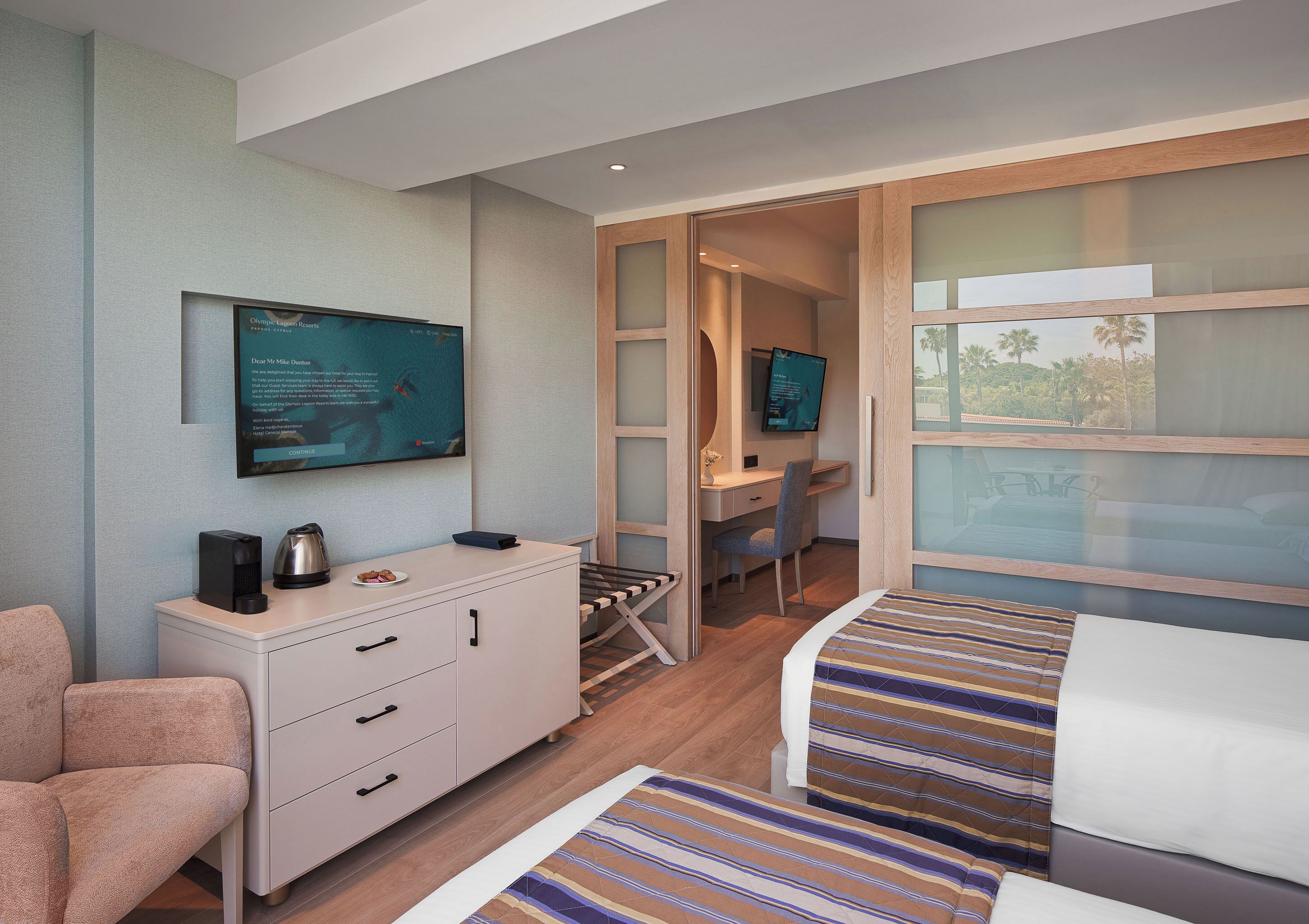 A hotel room with a bed, a desk, a chair, a dresser, a television, and a window with a view.