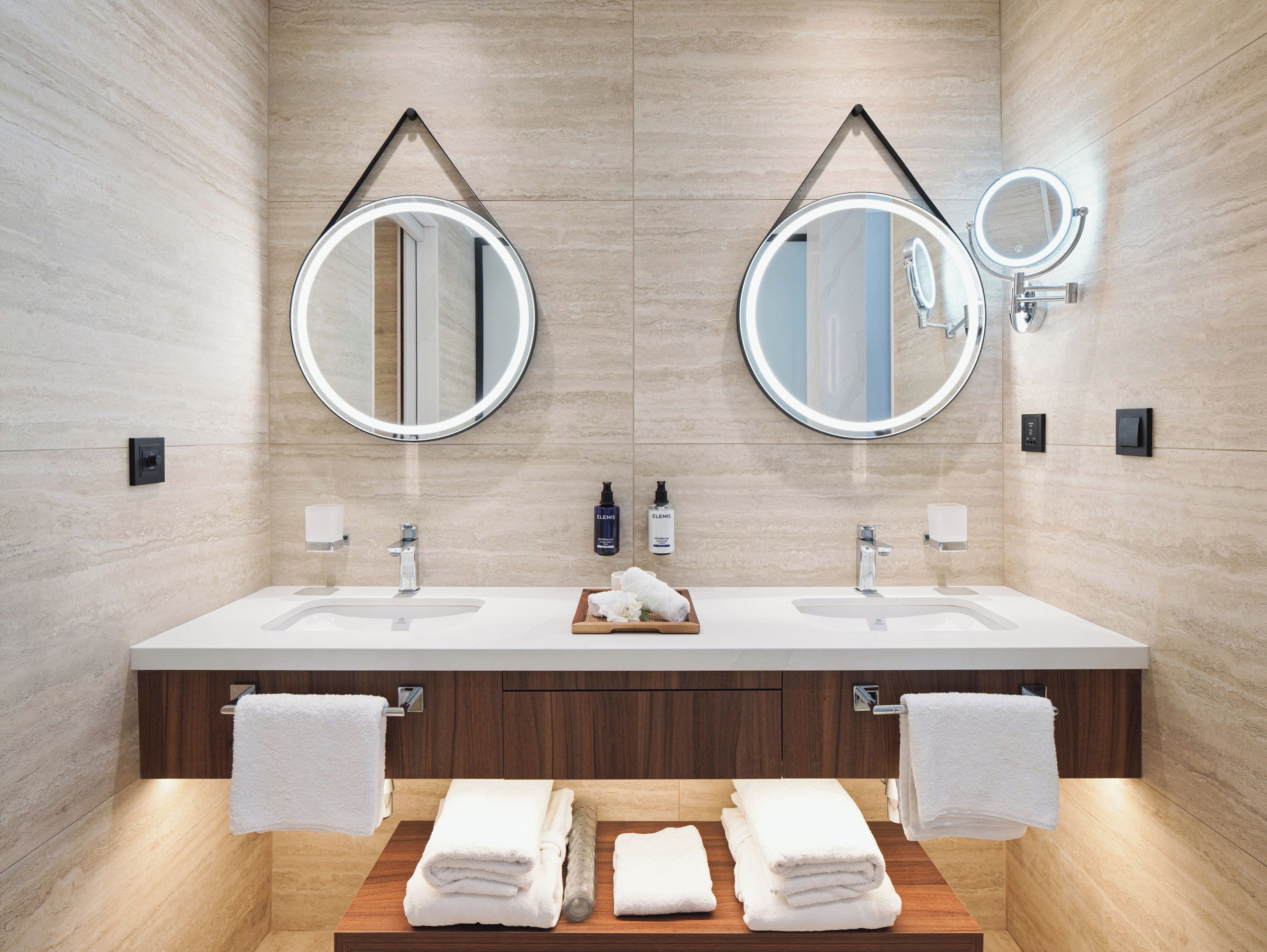 A modern bathroom with two sinks, large mirrors, and a wooden vanity.
