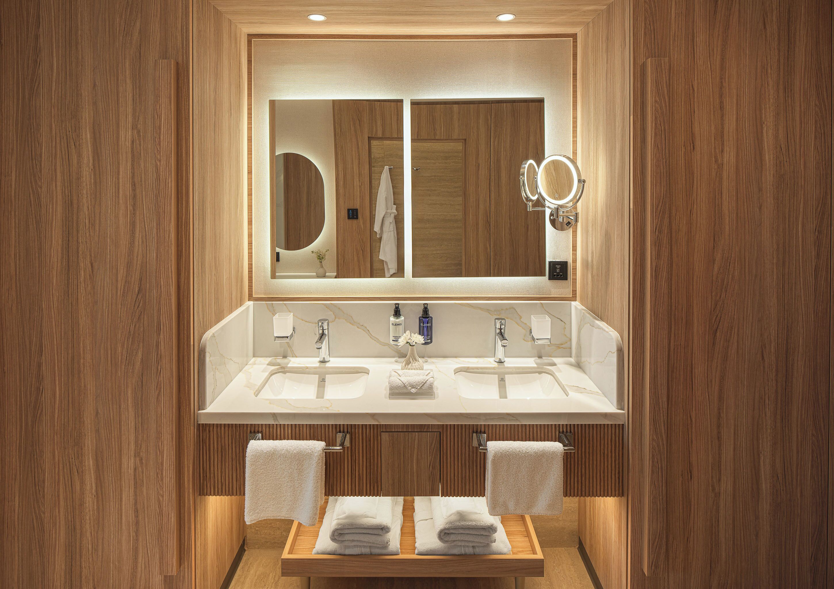 A modern bathroom with two sinks, a large mirror, and wooden paneling.