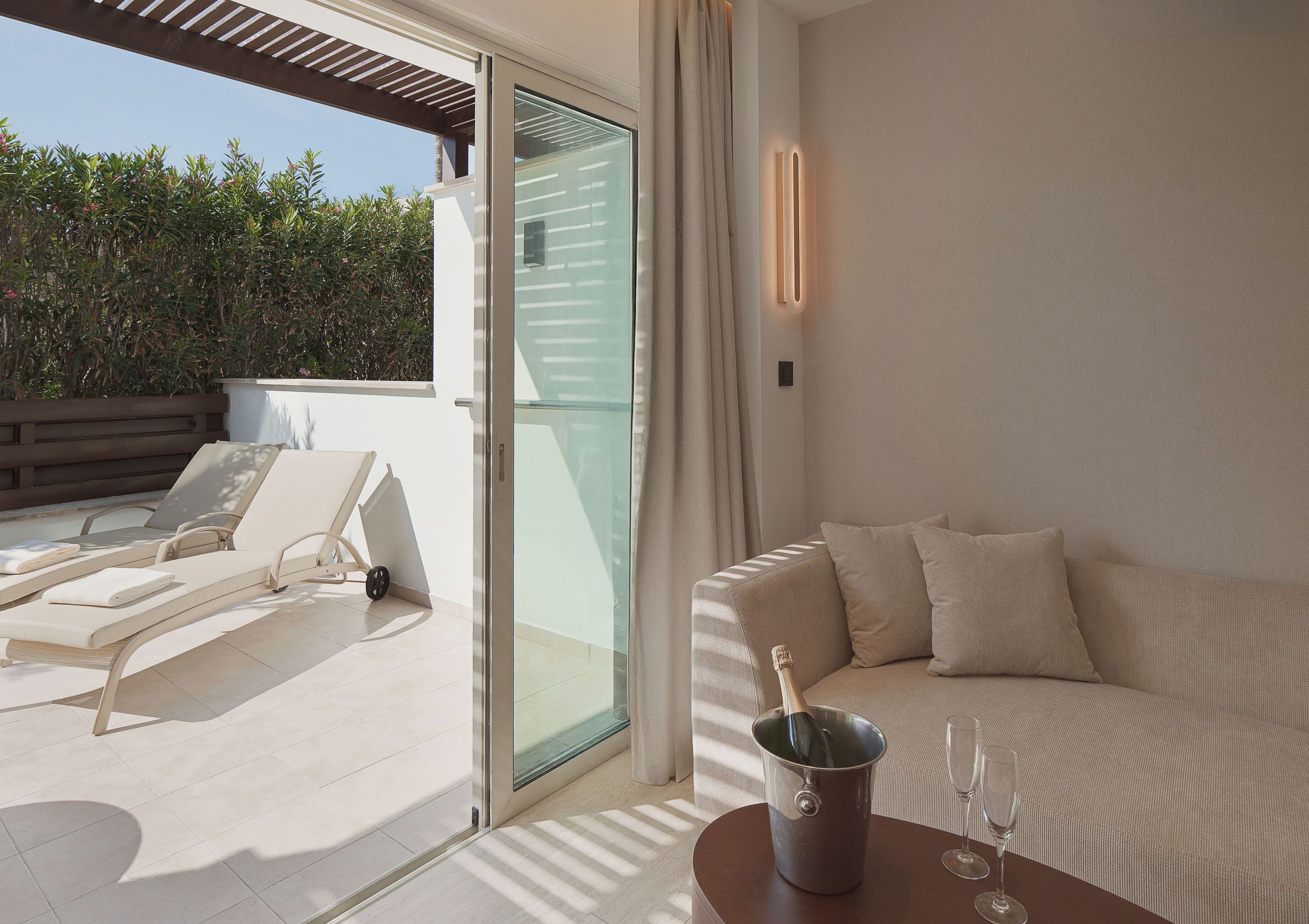 Une chambre d’hôtel moderne avec balcon, un canapé, une table avec un seau à champagne et des fauteuils de relaxation.