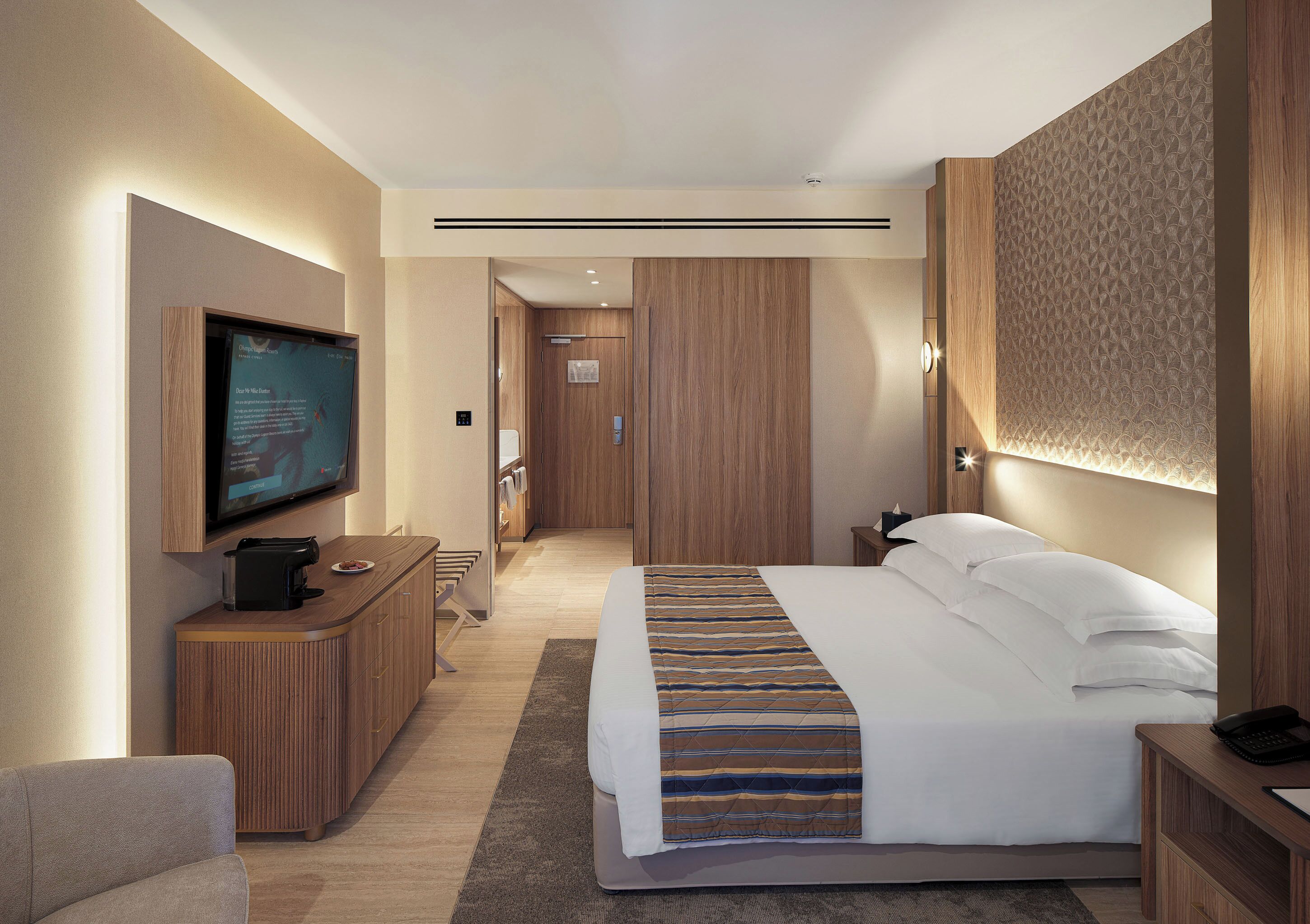 A modern hotel room with a large bed, a flat-screen TV, a desk, and a walk-in closet.