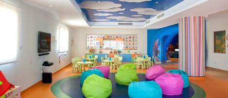A children's playroom with colorful bean bags, a play area, and educational posters on the walls.