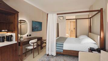 A bedroom with a four-poster bed, a desk with a chair, a coffee maker, and a mirror.