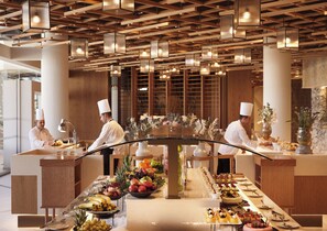 A modern hotel lobby with a central buffet table, wooden ceiling design, and staff in chef uniforms. - Olympic Lagoon Resort - Paphos - All inclusive (Paphos)