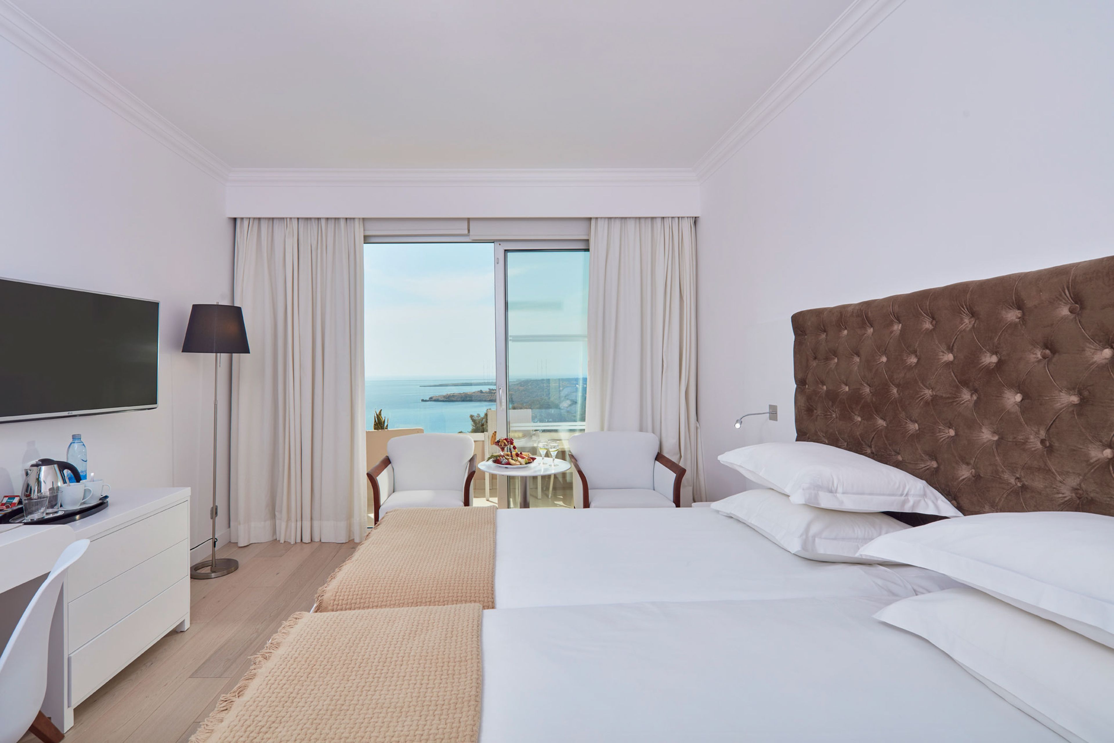 Habitación de hotel con una cama grande, un escritorio con televisor de pantalla plana, una mesita con una silla y un balcón con vistas al mar.