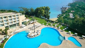 A resort with a large swimming pool, multiple sun loungers, and a view of the sea. - Grecian Park Hotel (Paralimni)